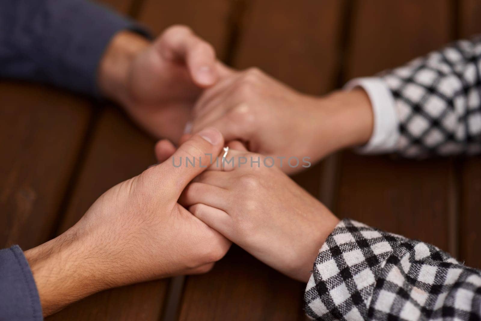 Close up on a man and a woman holding hands at a wooden table. Loving couple holding hands on table, man friend husband support woman wife expressing love feelings, trust care honesty in interracial relationship concept, close up view by Andrii_Ko