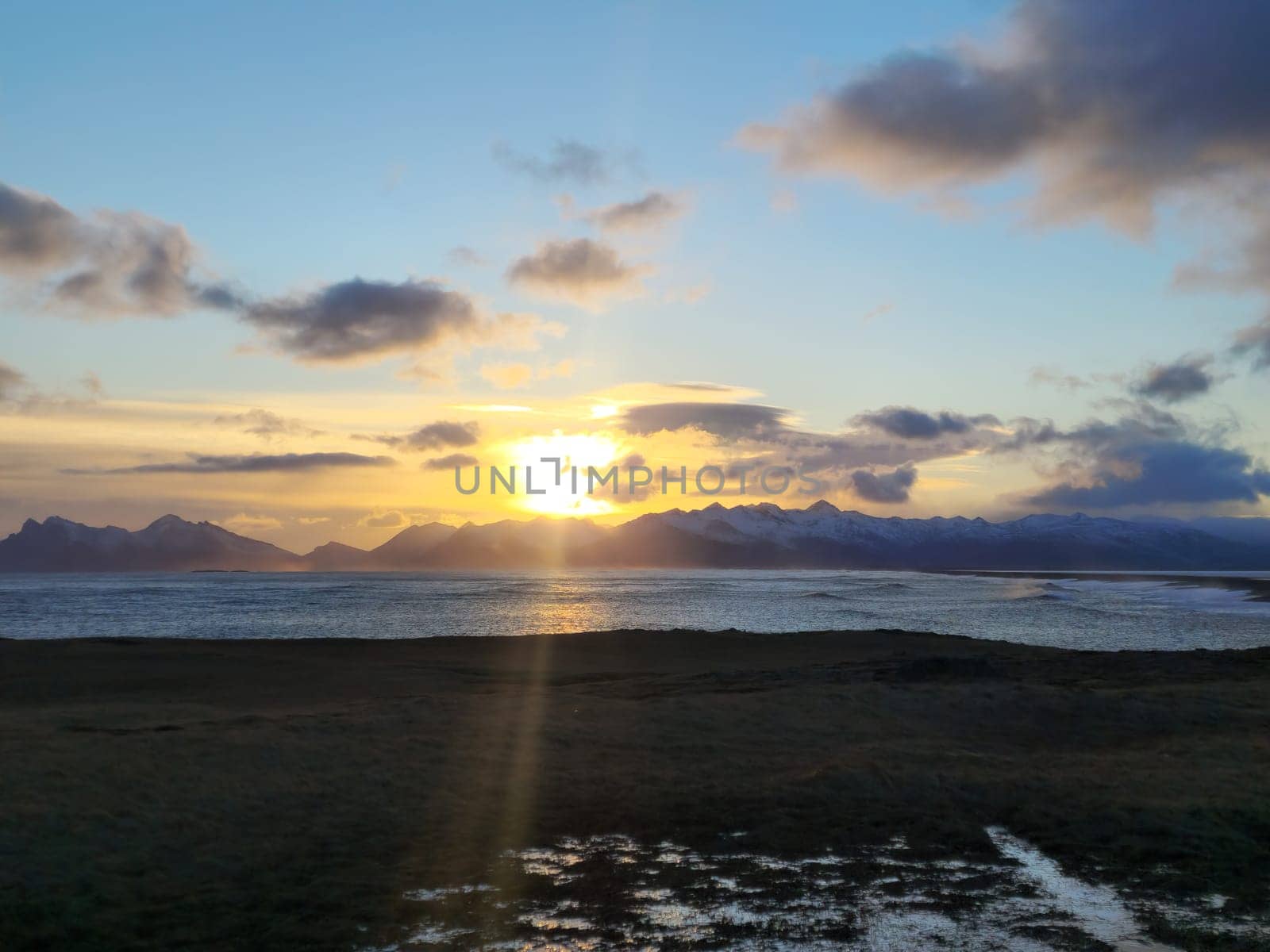 Arctic lake landscape at sunset with golden sky and snowy mountains, scandinavian wild nature creating fantastic scenery. Massive ocean beachfront around icelandic countryside.