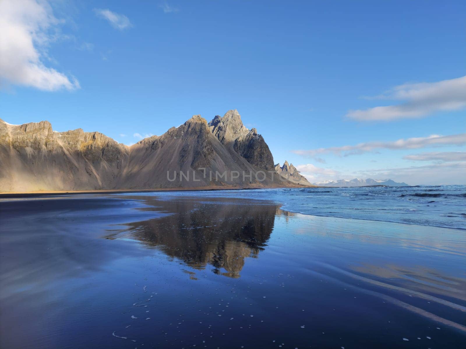 Massive vestrahorn mountains scenery with natural black sand beach on stokksnes peninsula. Atlantic ocean beachfront hosting rocky mountain crest creating majestic coastline landscape.