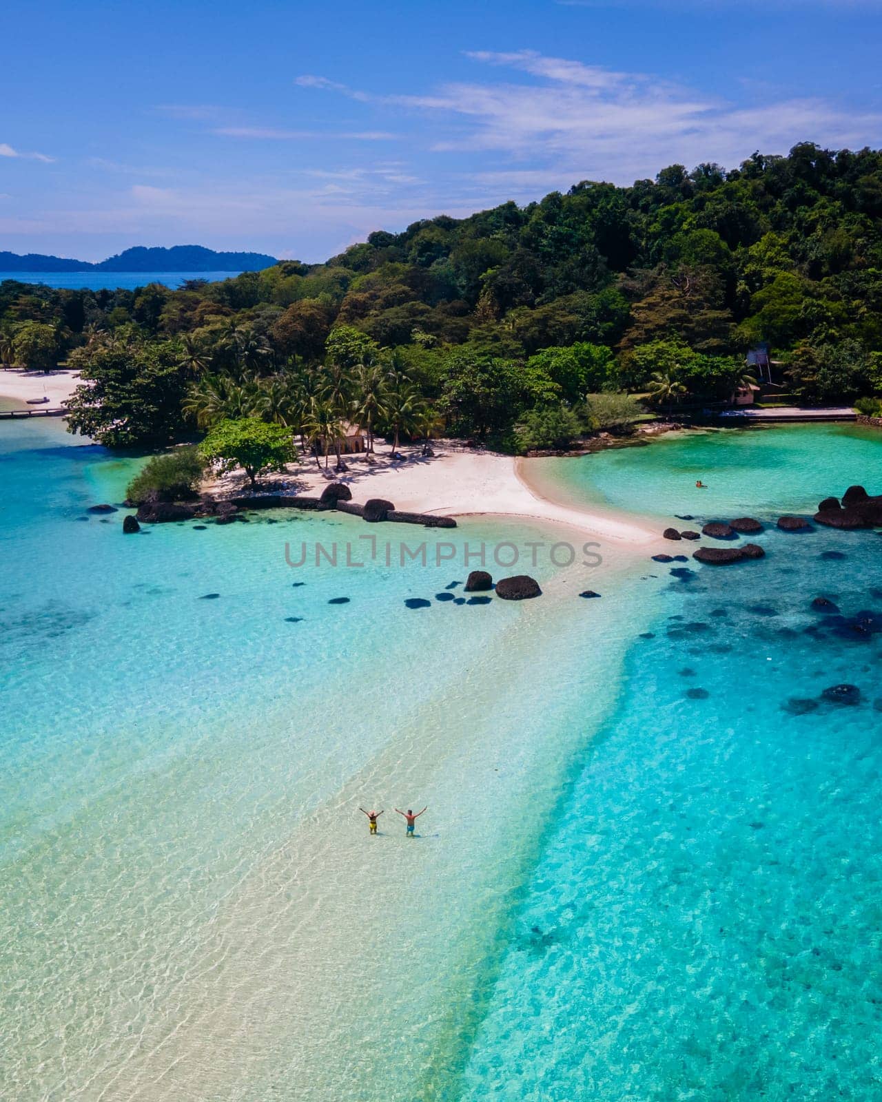 couple walking at the beach of Koh Kham Trat Thailand, aerial drone view of the tropical island near Koh Mak Thailand. white sandy beach with palm trees and big black boulder stones in the ocean