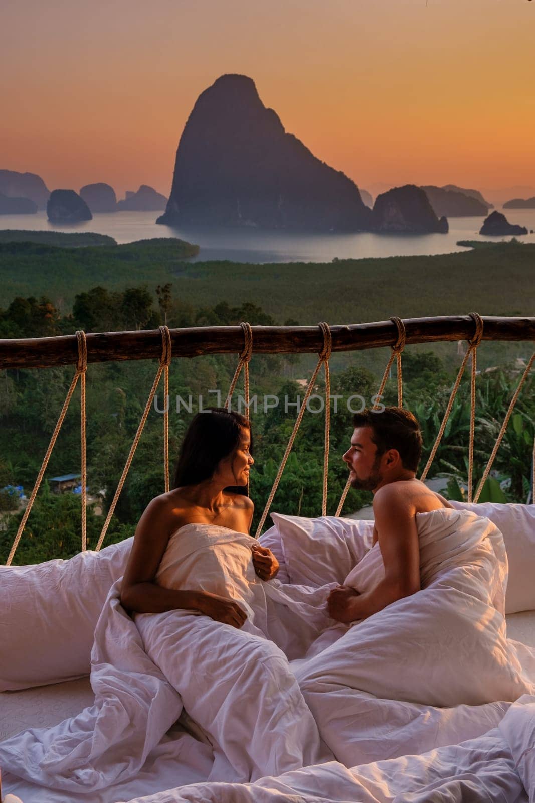 A couple in an outdoor bedroom watching the sunrise over Sametnangshe mountains in Phangnga Bay Thailand