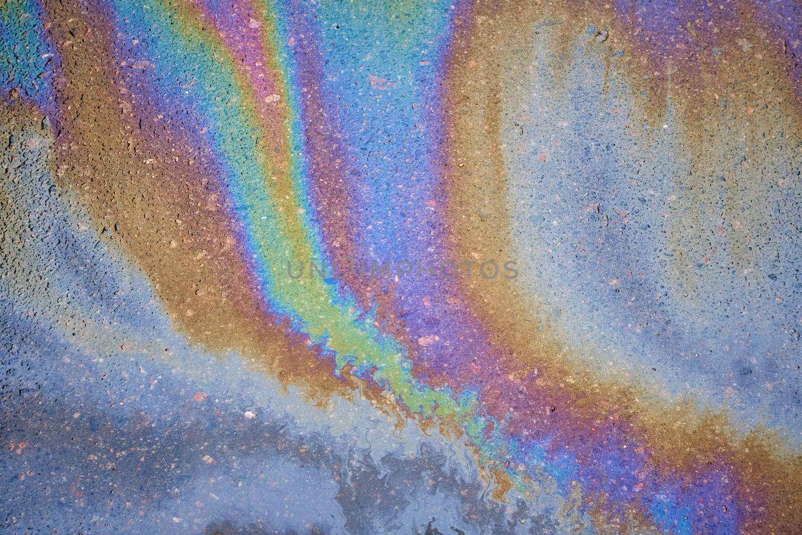 Gasoline spot on wet asphalt. Multi colored oil spill on asphalt road, abstract background, texture.