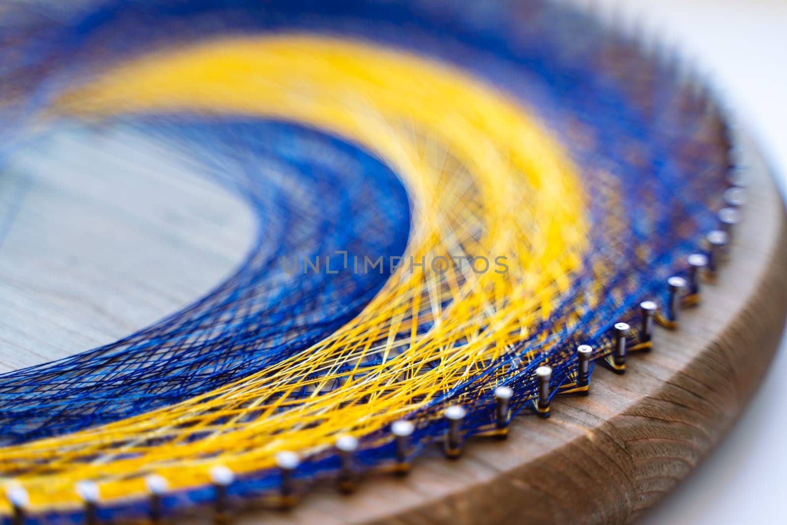 Colored thread mandala on a wooden board with nails. Mandala Moon Harmony Sun esotericism and psychology pictures from yellow and blue silk threads