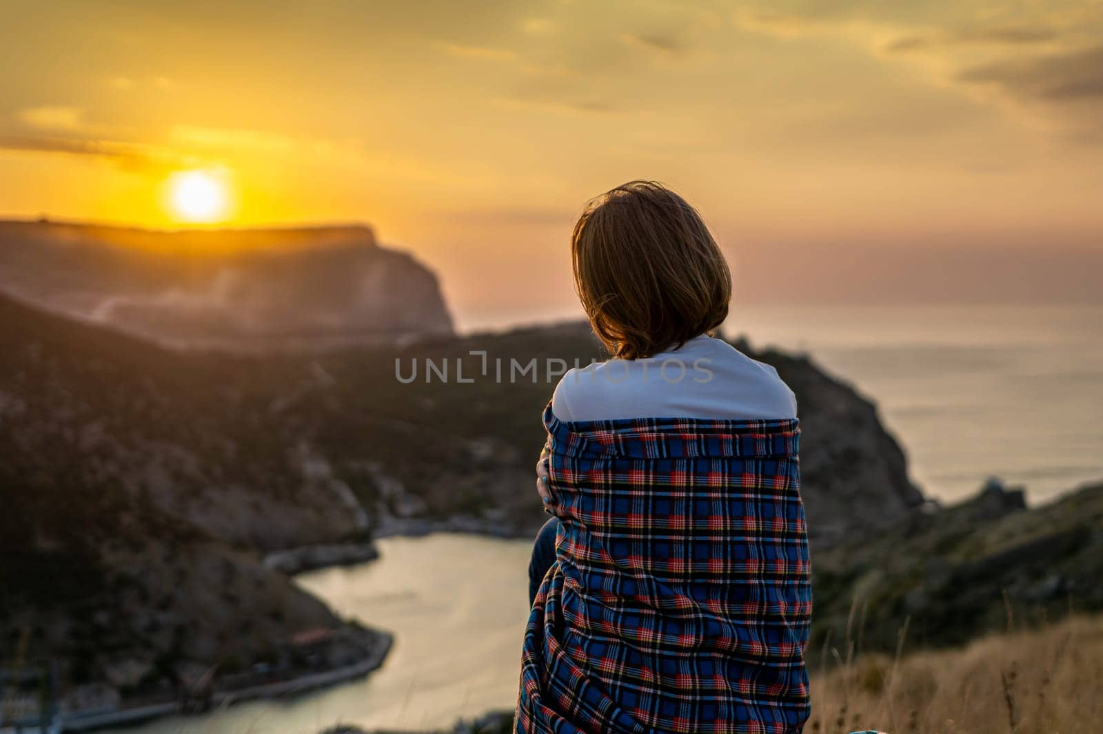 Happy woman on sunset in mountains. Woman siting with her back on the sunset in nature in summer. Silhouette. by Matiunina