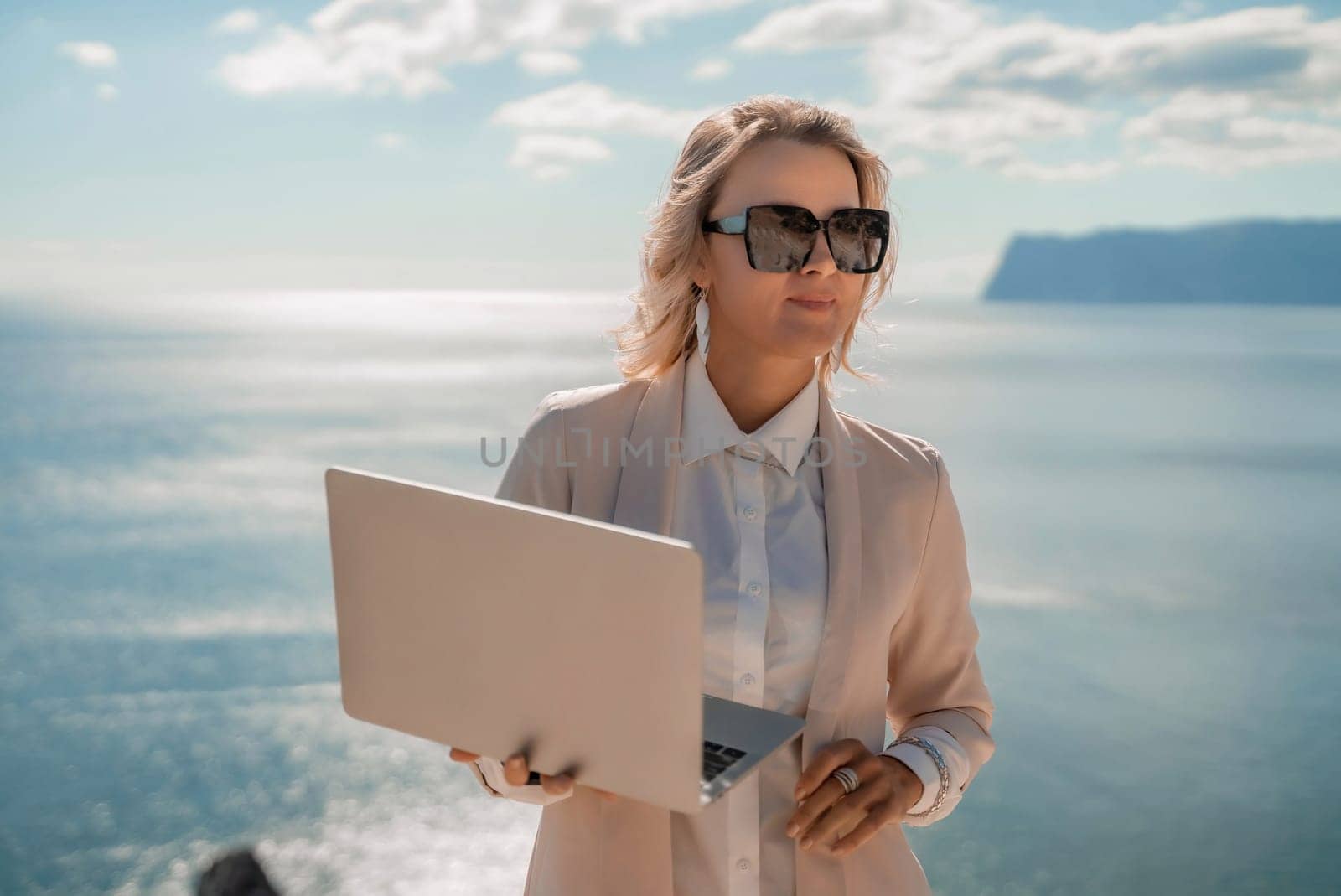 Freelance women sea. She is working on the computer. Good looking middle aged woman typing on a laptop keyboard outdoors with a beautiful sea view. The concept of remote work