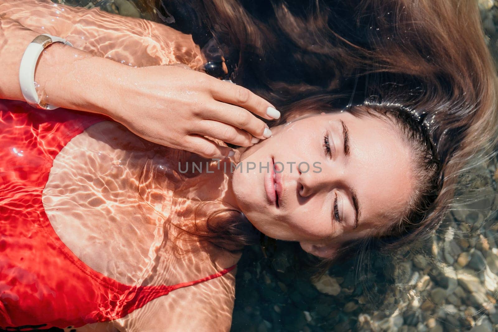 Woman travel portrait. close-up portrait of a happy woman with long hair in a red bikini, floating in water and smiling at the camera. by panophotograph