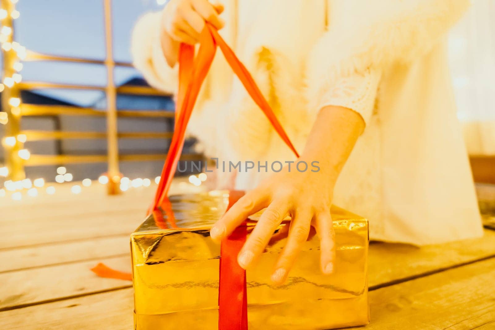 A woman in a white dress is holding a gold box with a red ribbon. She is wearing a crown on her head. The woman appears to be opening the gift box. by panophotograph