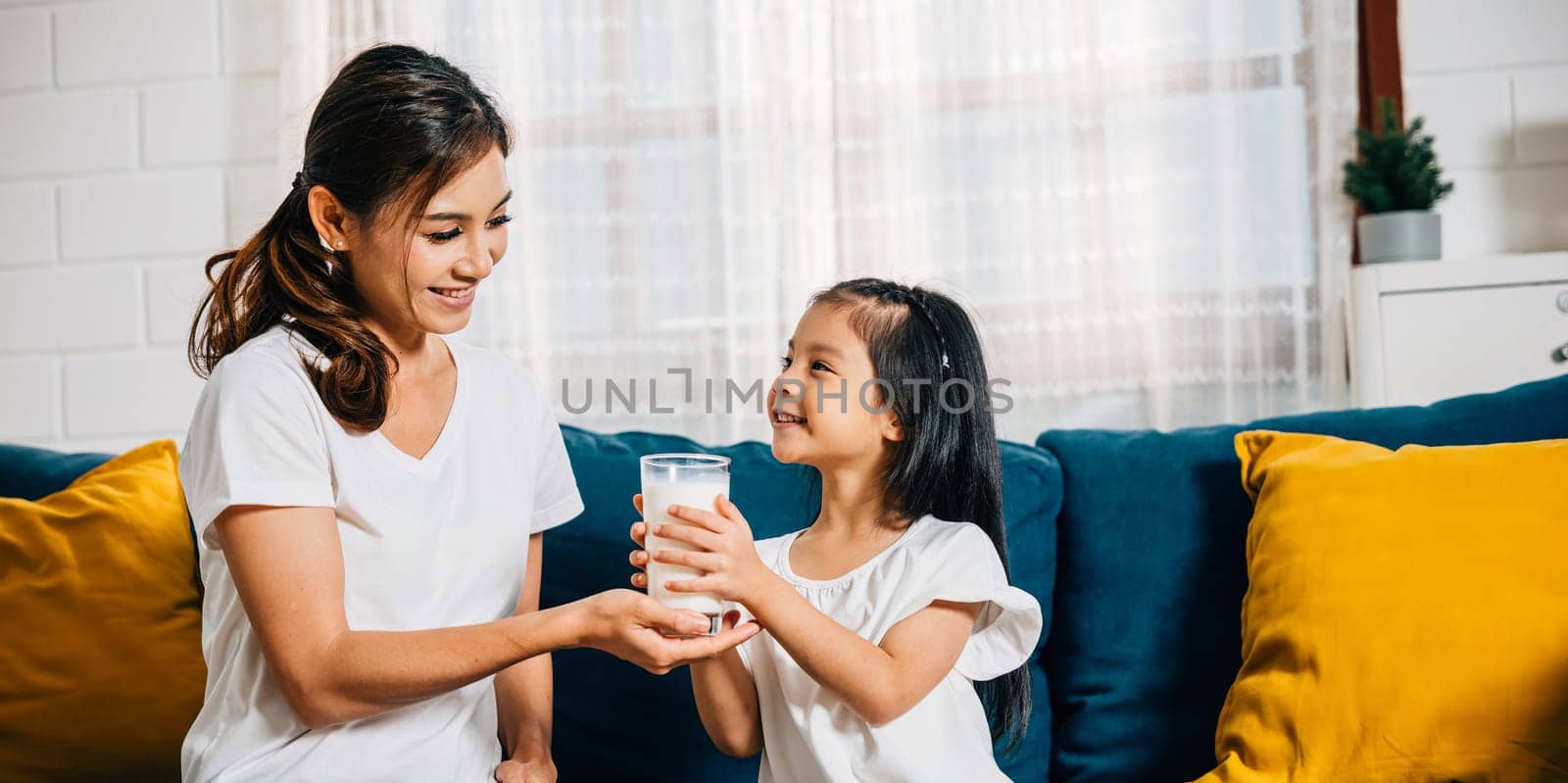 A beautiful family morning as an Asian mother gives her daughter a glass of milk by Sorapop