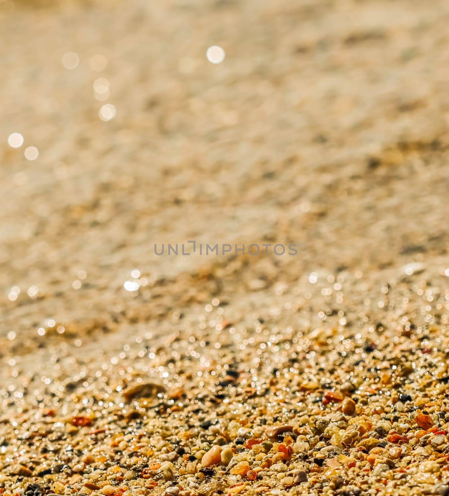A background of sand, small pebbles and flowing waves on the sea beach. Summer vacation and coastal nature concept