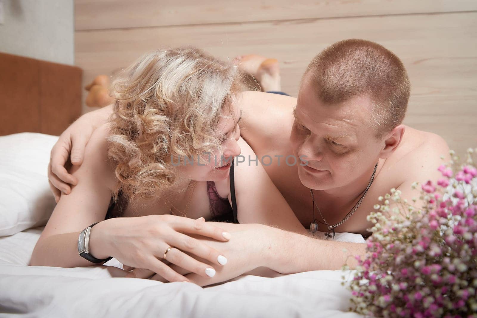 Loving enamored adult couple communicates, embraces, and has fun alone together on the bed in the bedroom or hotel room. The woman is wearing tank top and the man is shirtless