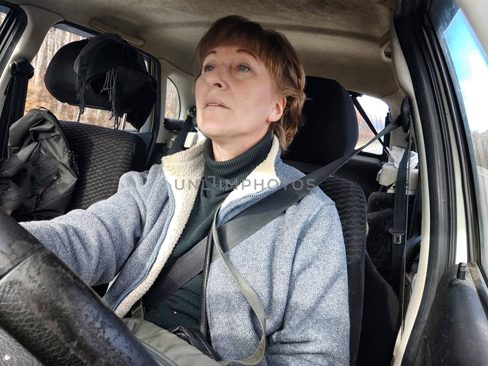 Portrait of female driver in solo journey. Adult mature woman holding steering wheel and looking through windscreen in travel by vehicle on vacation. Lady girl who is owner or rent a car for travel by keleny