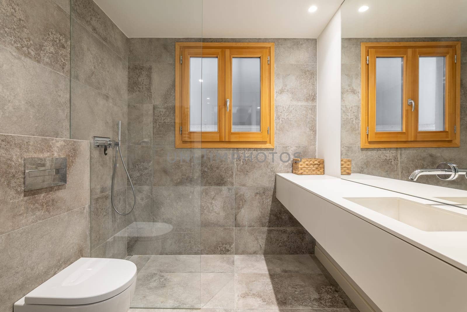 Large bathroom with long vanity unit near washbasin area. Light washing area with expensive tiles and wooden inner window reflect in large mirror