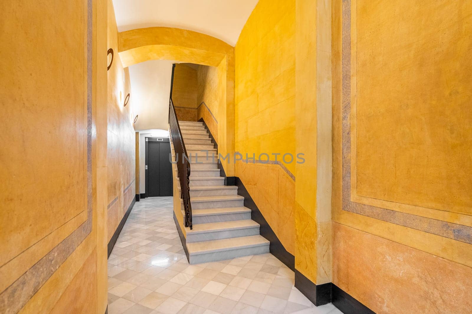 Stairs in yellow-walled hallway at entrance of dwelling building. Striking design solution for hotel renovation. Place to rest on vacation