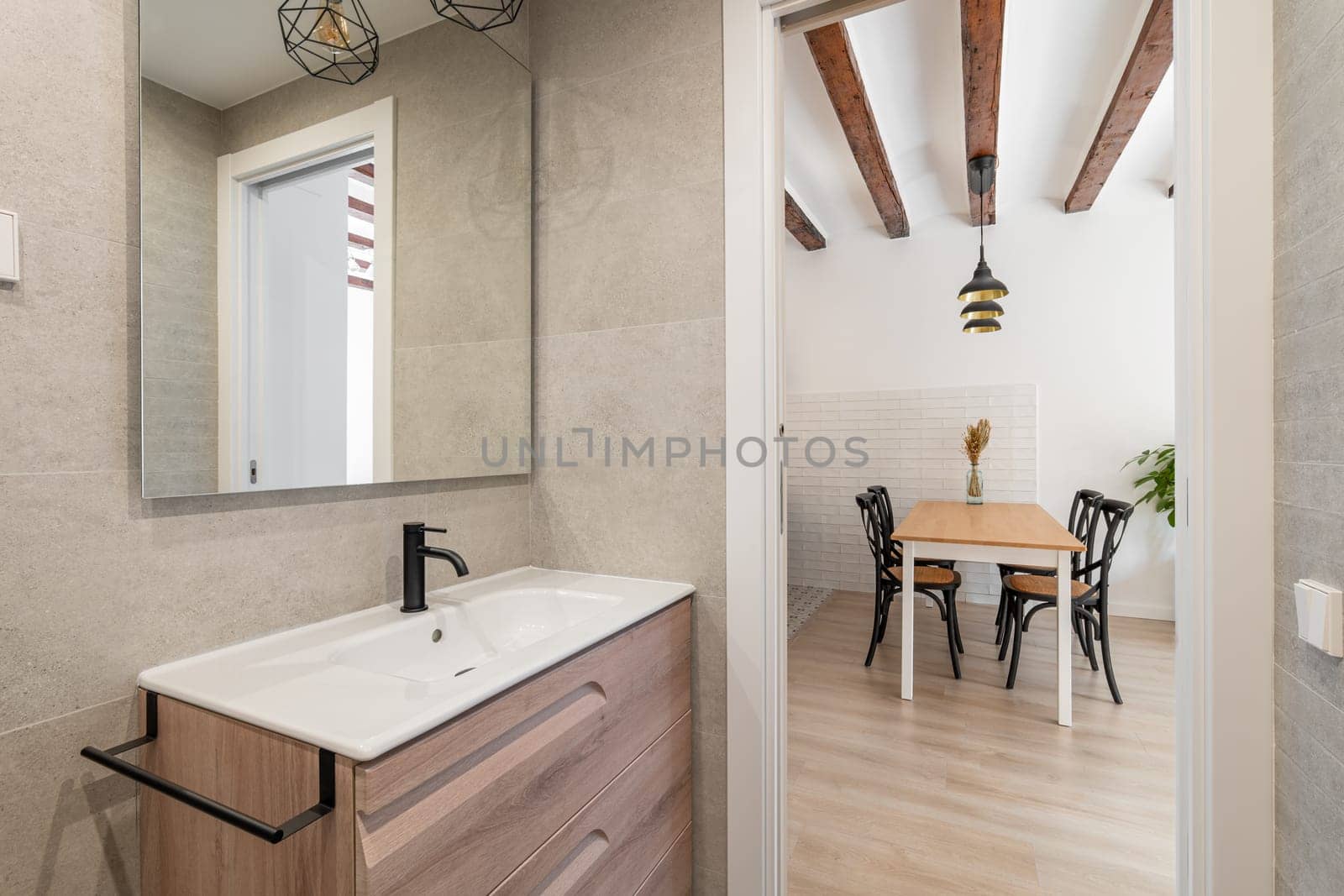 View from the bathroom with a sink and a mirror to the kitchen living area with a table and chairs waiting for the tenants. Concept of real estate and the work of realtors with new apartments by apavlin