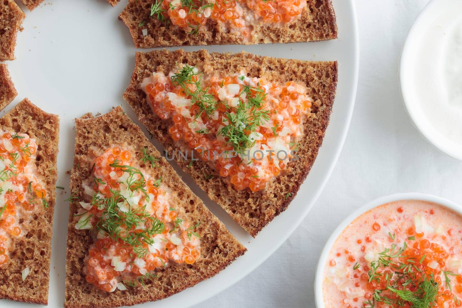 Homemade appetizer with red caviar, sour cream, dill, onion and rye bread on the white table - the traditional finnish recipe for a holiday food, flat lay in minimalistic style, healthy eating concept, horizontal