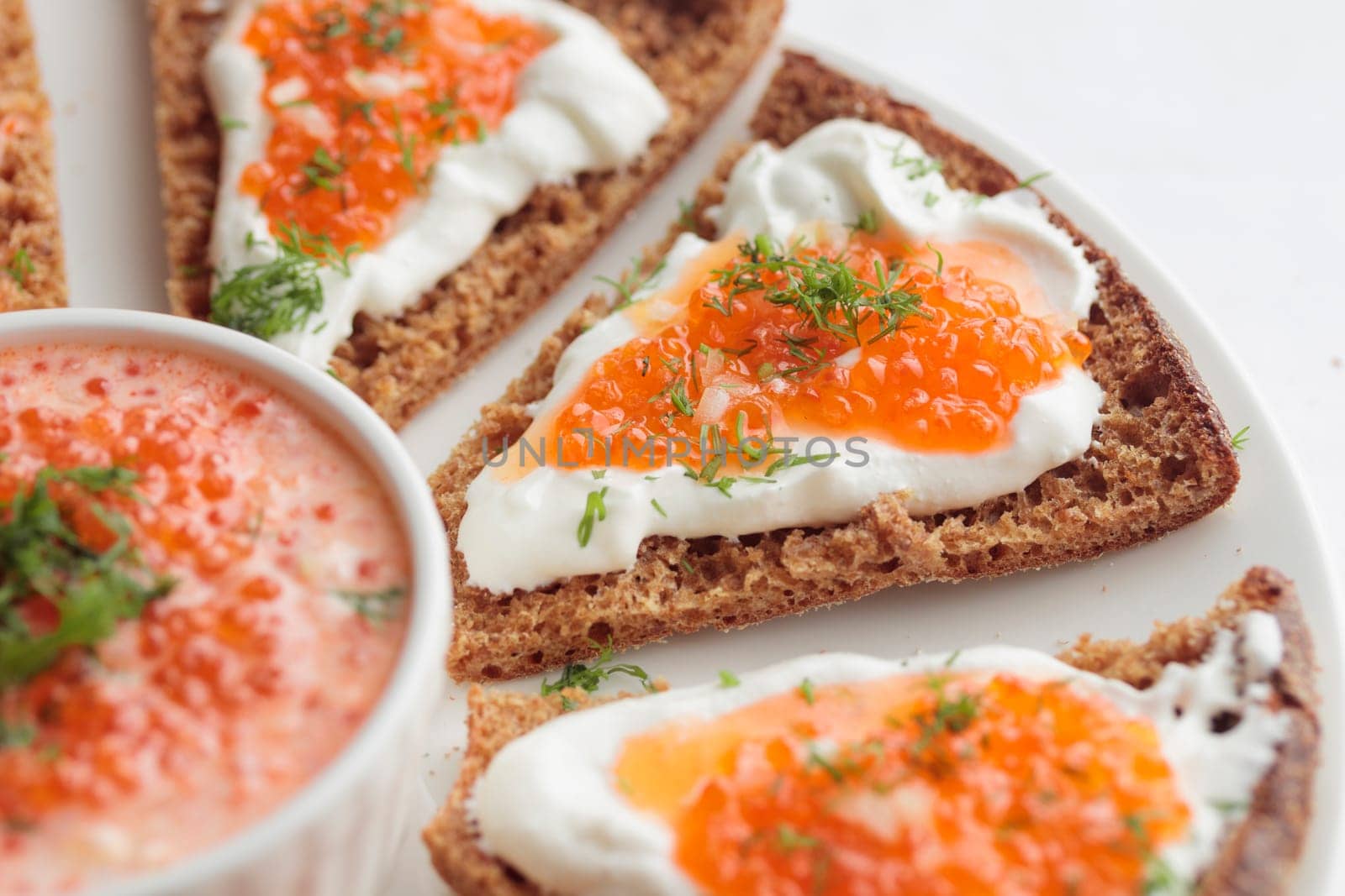 Homemade appetizer with red caviar, sour cream, dill, onion and rye bread on the white table - the traditional finnish recipe for a holiday food, flat lay in minimalistic style, healthy eating concept, horizontal