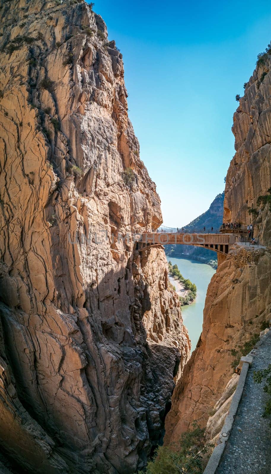 Stunning view of King's Pathway in Malaga featuring a bridge over a ravine and anonymous tourists trekking, with room for text in the blue sky.