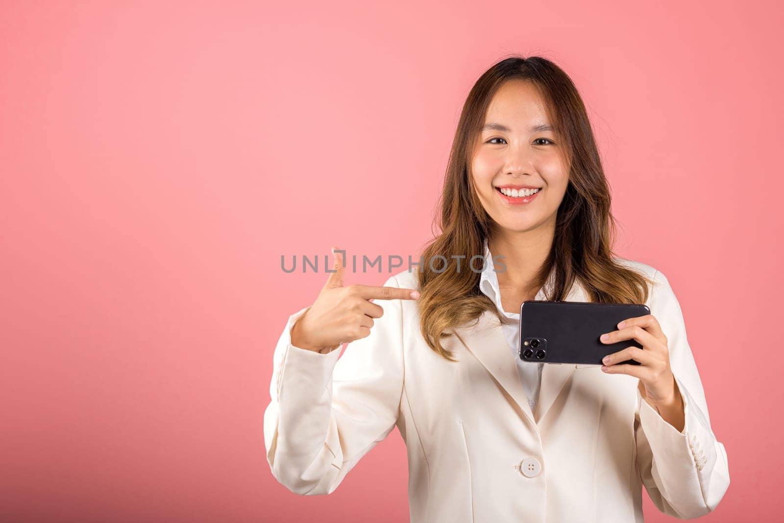 Portrait Asian happy beautiful young woman smile making finger pointing on screen smartphone in hand, female attractive shopping online application isolated studio shot pink background with copy space