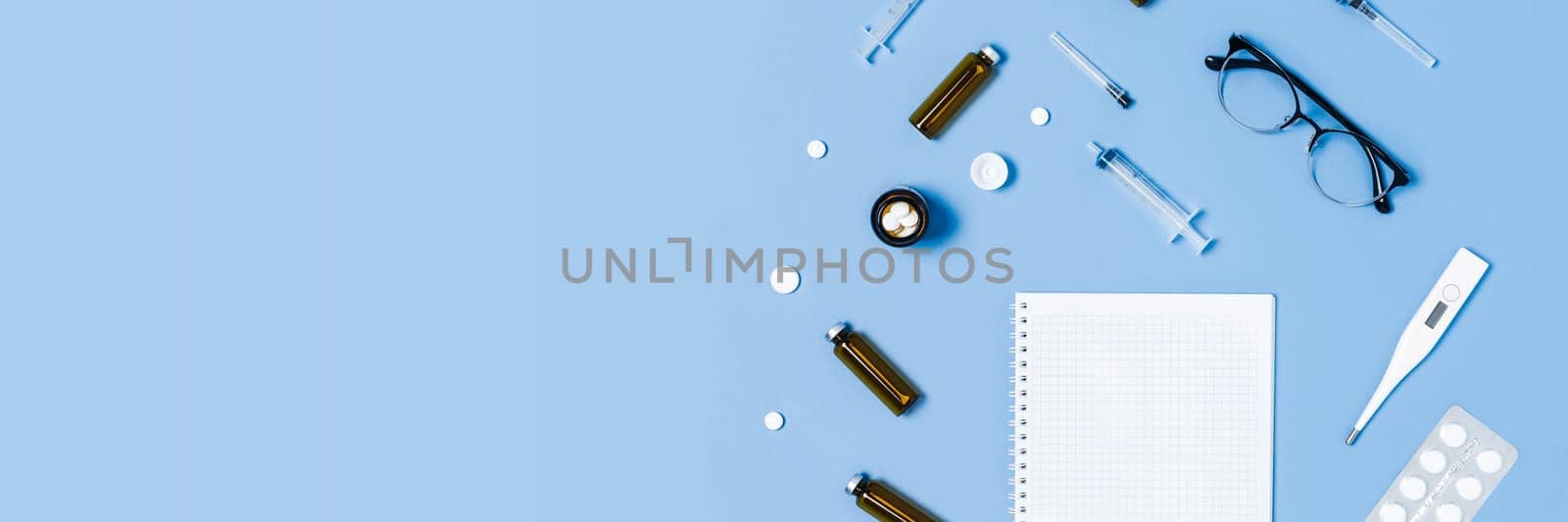 Medical blue background with different accessories: stethoscope, thermometer, syringe, tablets and notepad.