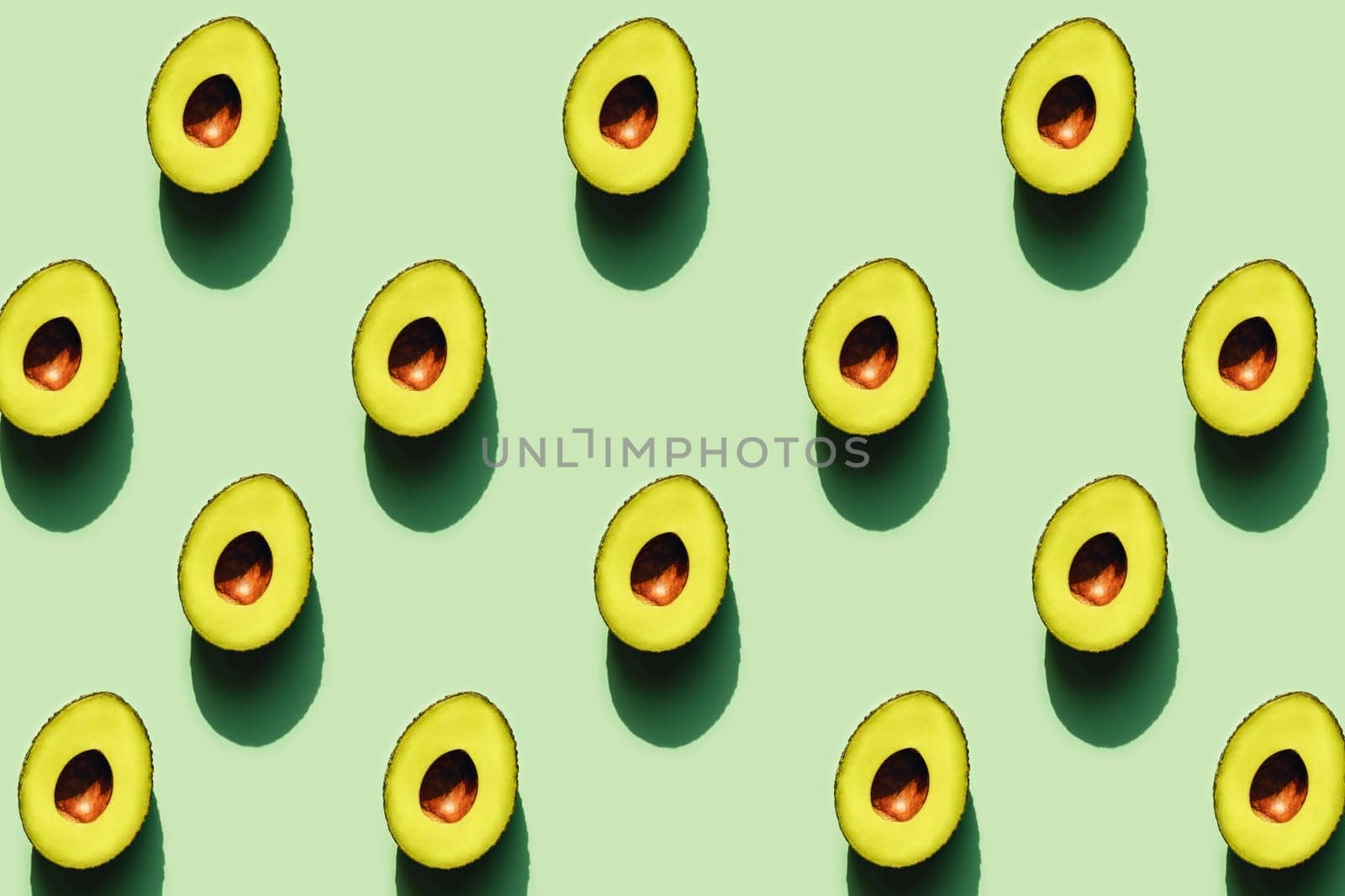 Half of avocados in sunlight on a green neon background.