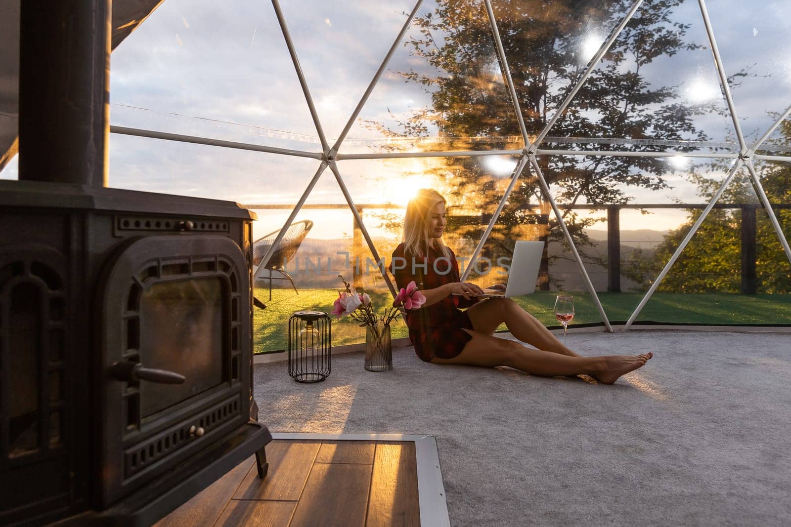 Woman working on laptop geo dome tents. Green, blue background. Cozy, camping, glamping, holiday, vacation lifestyle concept. Outdoors cabin, scenic background.