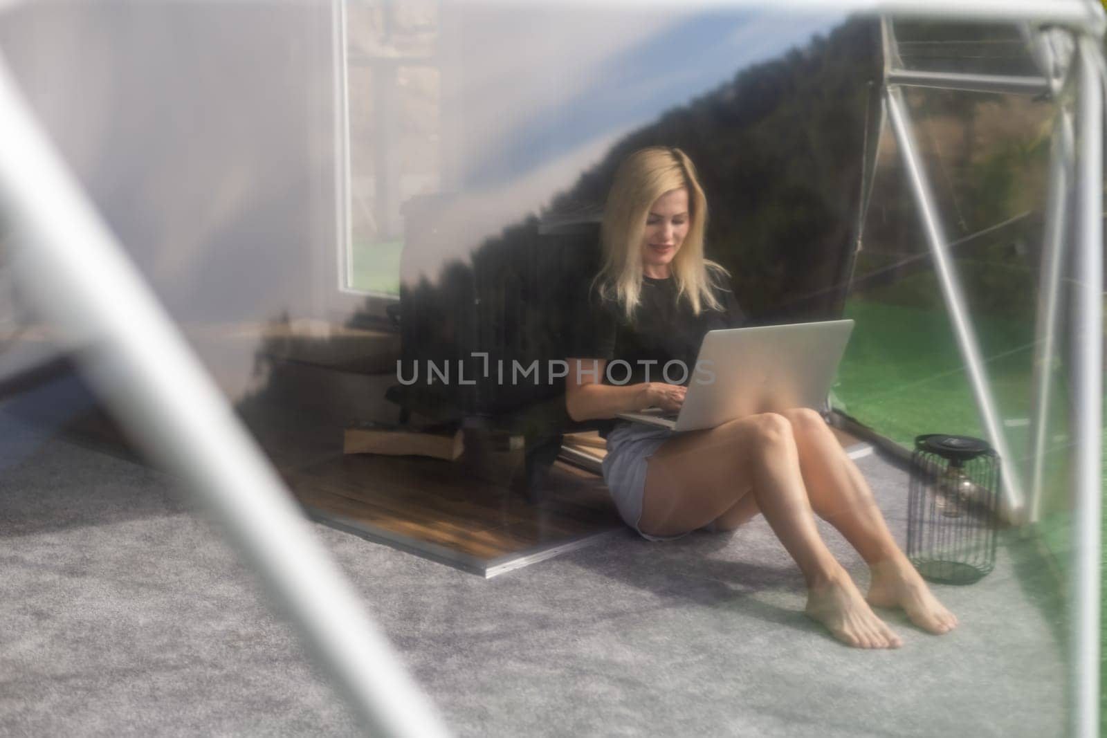 Young caucasian woman using and watching on laptop computer on in dome camping hotel. Tourism, vacation and weekend