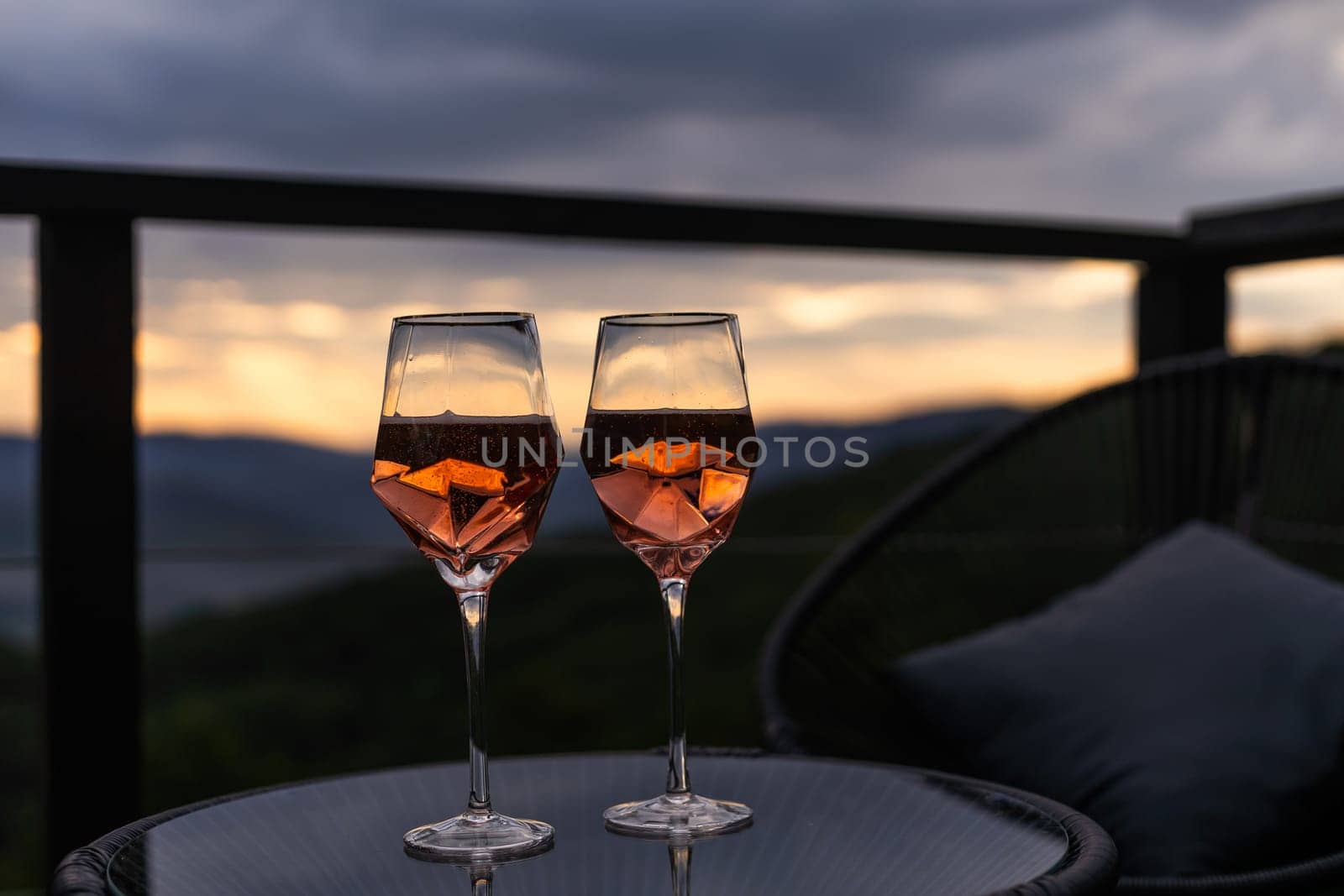 Champagne and cocktail glasses on glass table outdoor patio overlooking mountains at sunset.