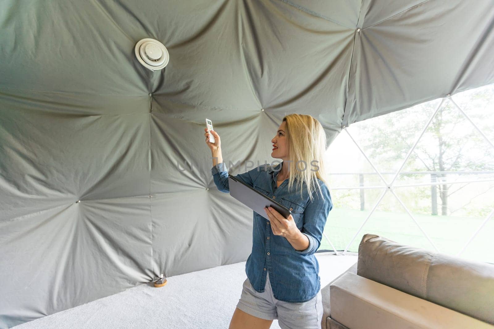 Young woman using smartphone home application on tablet computer when setting temperature in her apartment by Andelov13