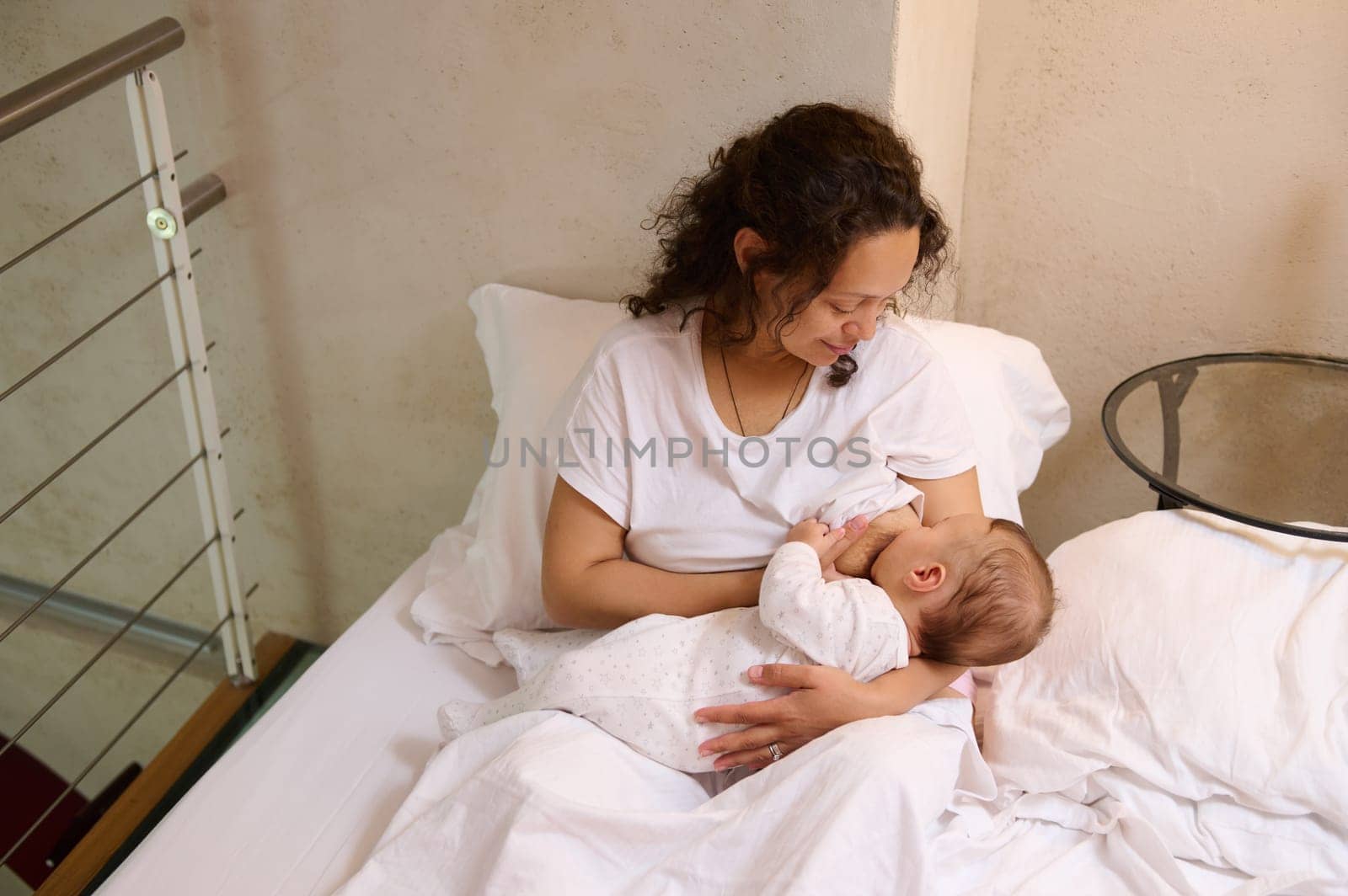 Overhead view of mother breastfeeding her newborn baby in the bedroom. Milk from mother's breast is a natural medicine for children. Breastfeeding as a way to reduce the risk of breast cancer
