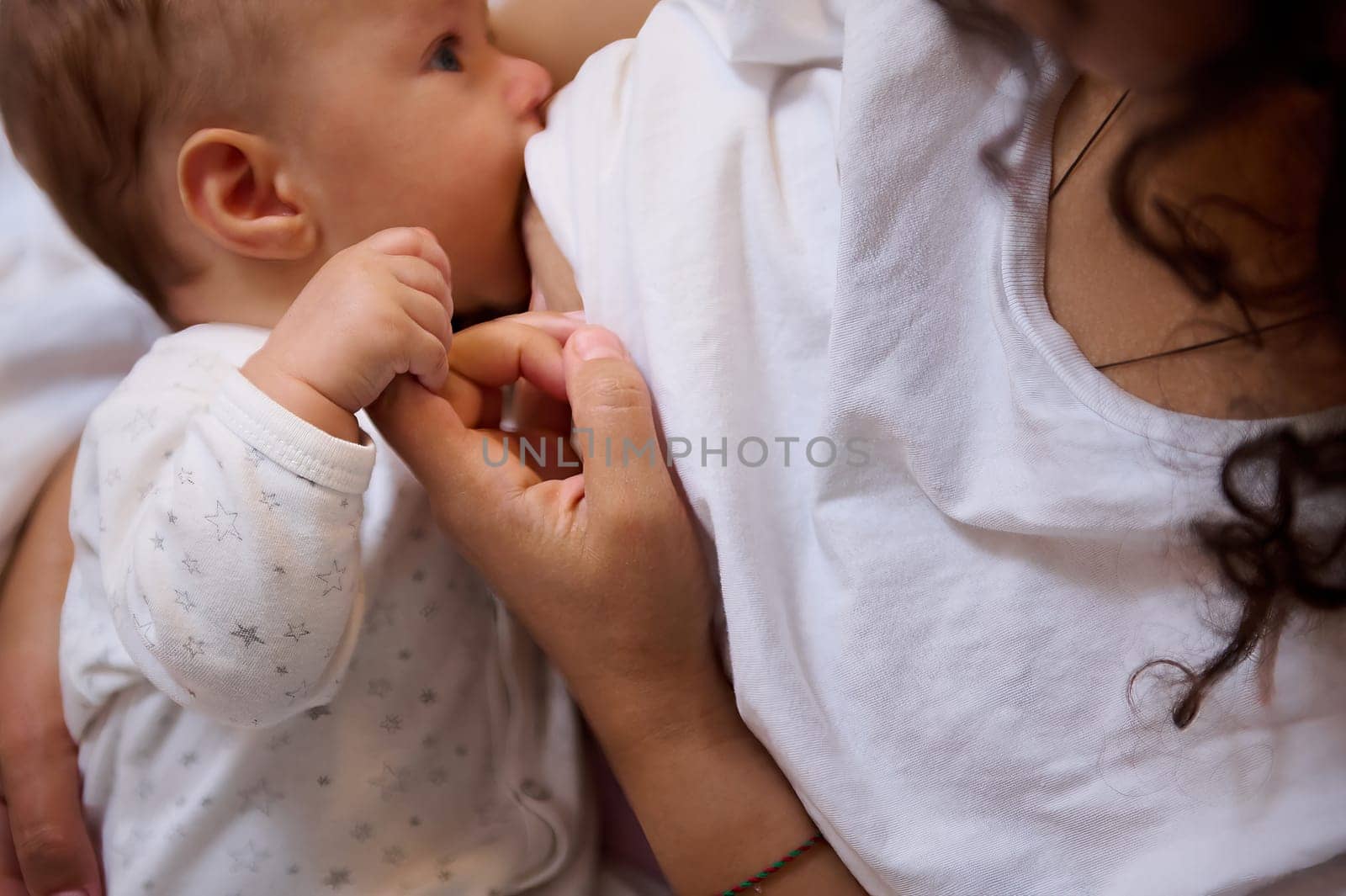 Close-up of a loving caring mother breastfeeding her baby boy. View from above of a cute child suckling the milk of his mom. Family relationships. Maternity lifestyle and infancy.