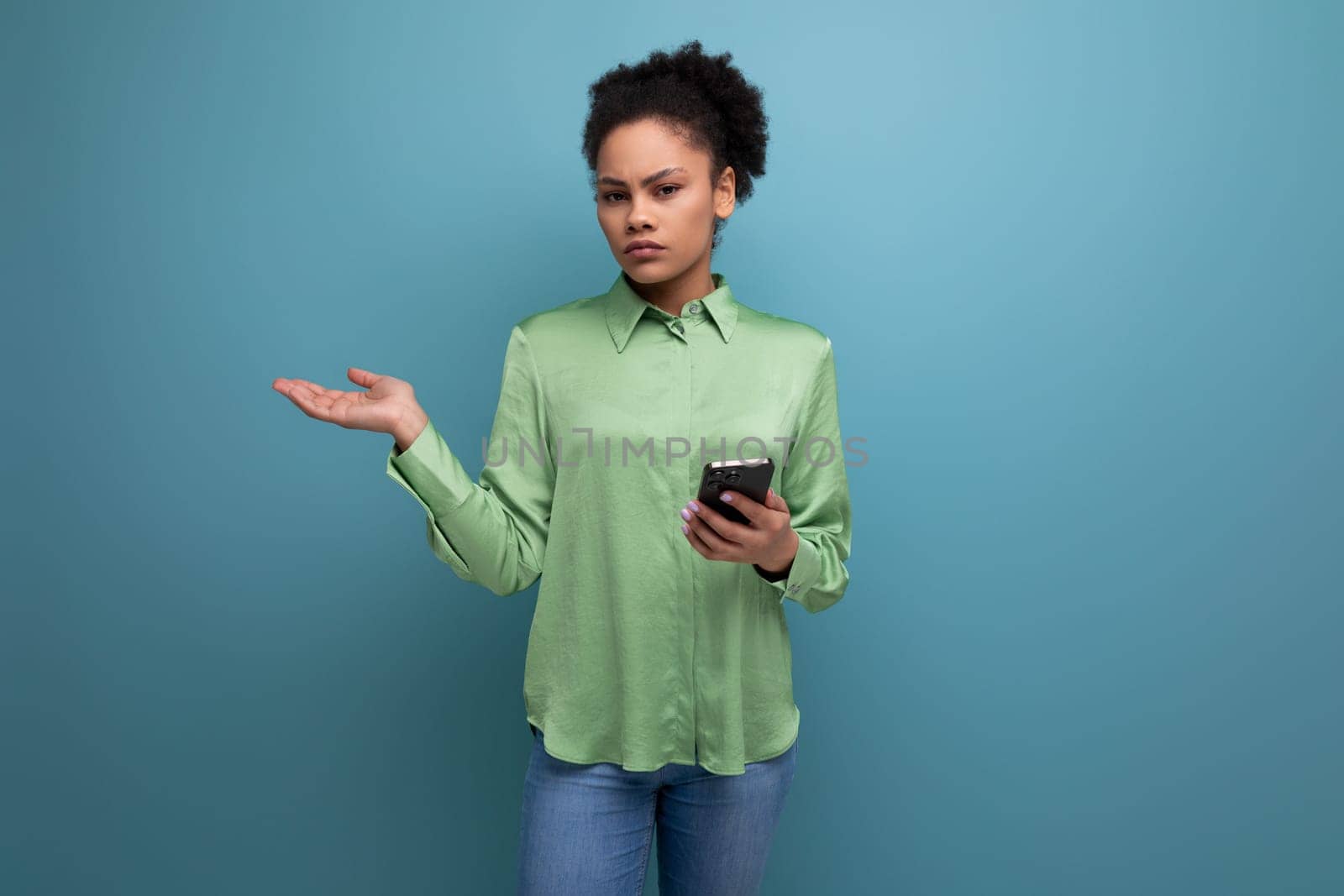 a young brunette hispanic woman with curly hair dressed in a green blouse holds a phone in her hand against the background with copy space. people lifestyle concept by TRMK