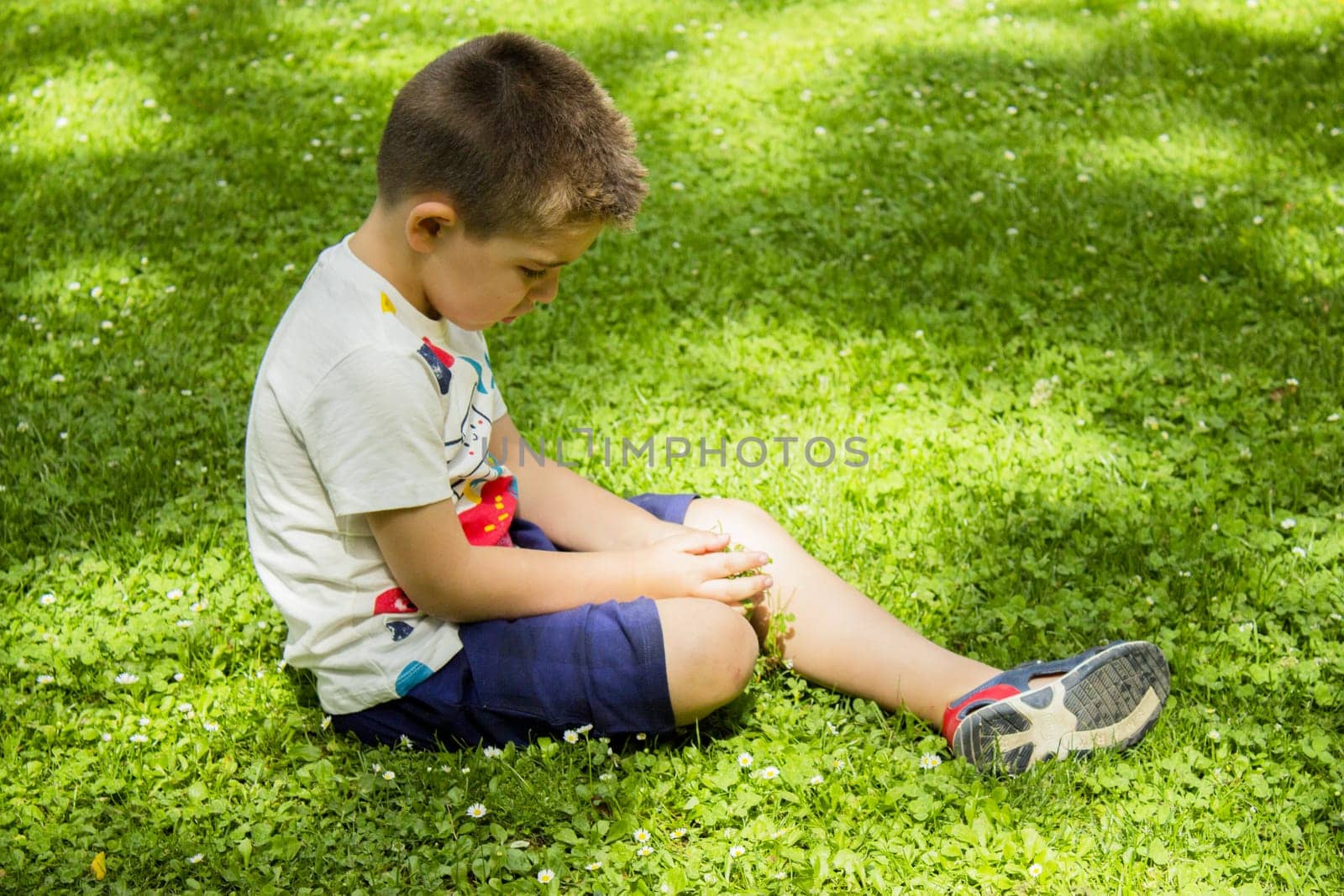 Four year old boy sitting on the grass pensive by GemaIbarra