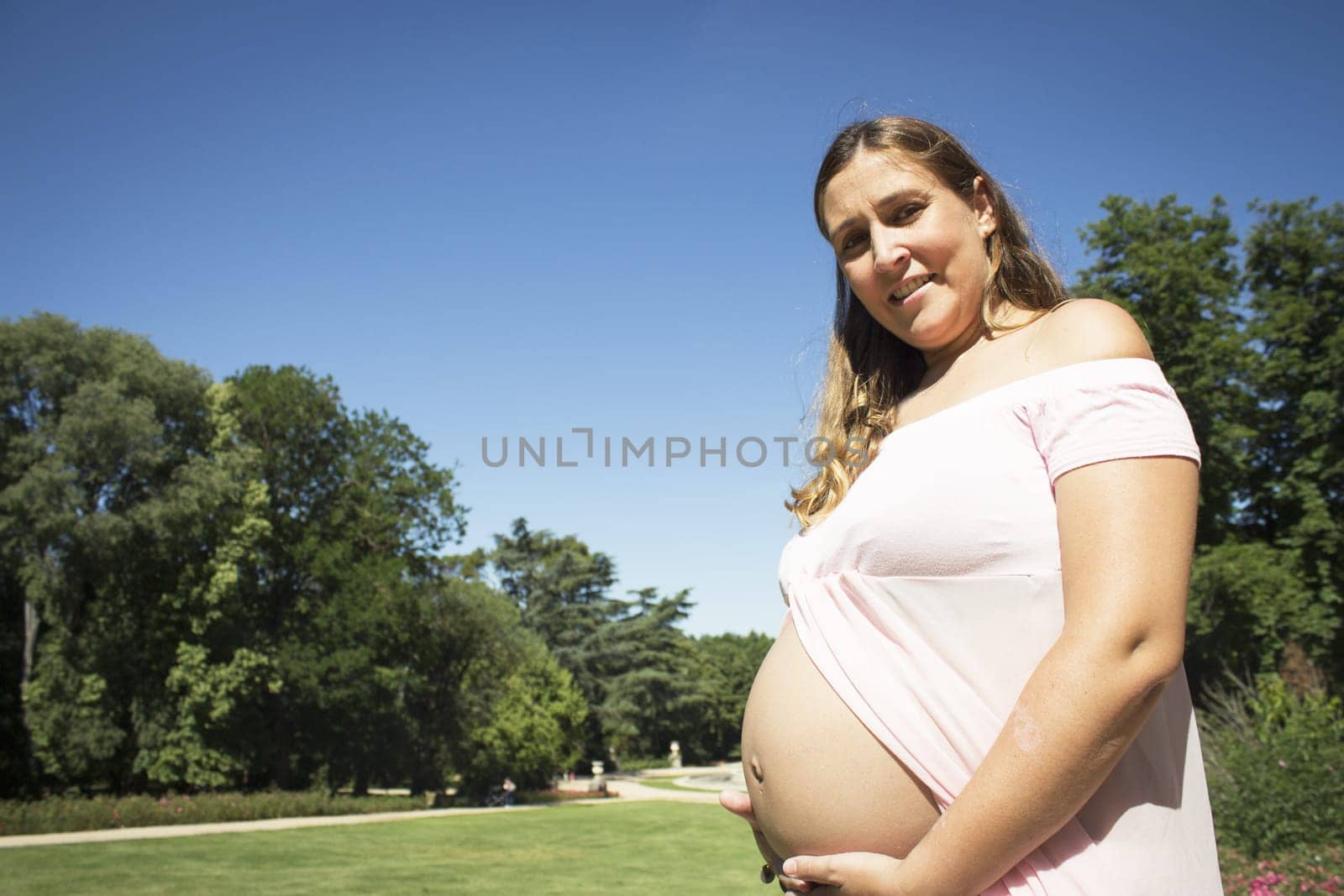 Seven month pregnant woman standing dressed in pink. Happy expression