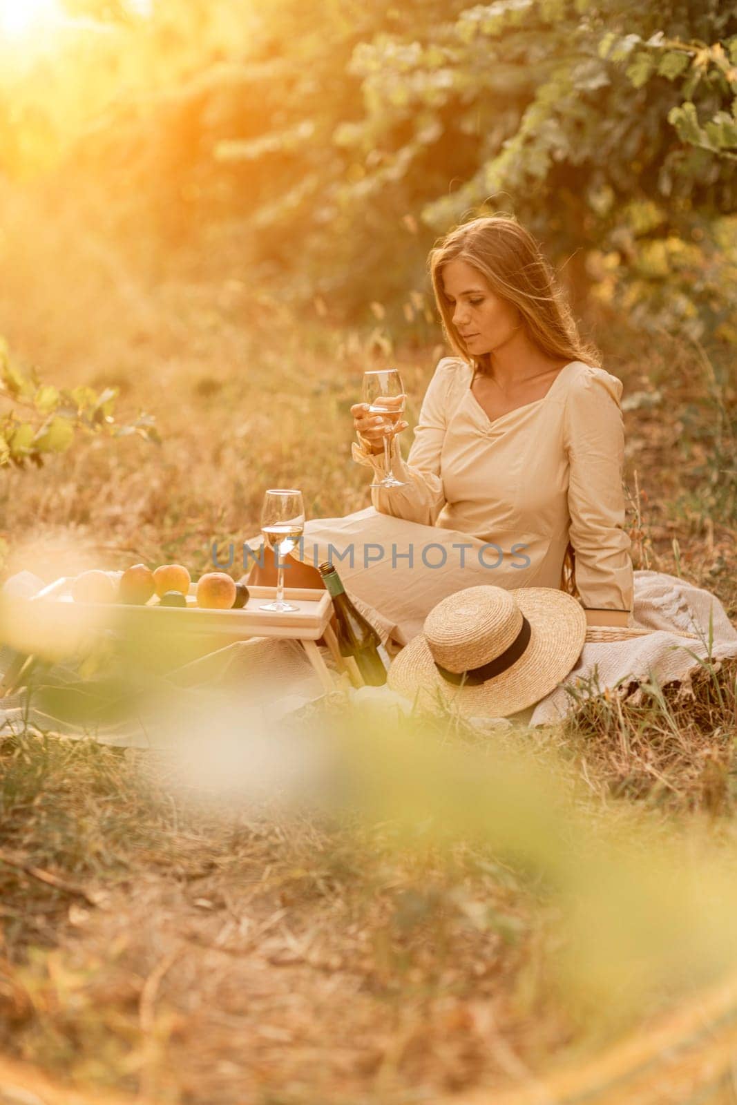 Woman picnic vineyard. Romantic dinner, fruit and wine. Happy woman with a glass of wine at a picnic in the vineyard on sunny day, wine tasting at sunset