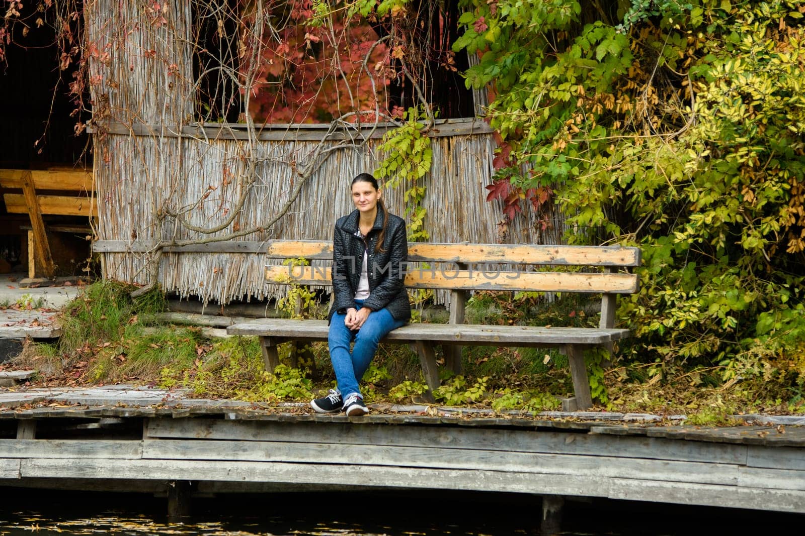 A young beautiful girl in casual clothes sits on a bench in an autumn park by Madhourse