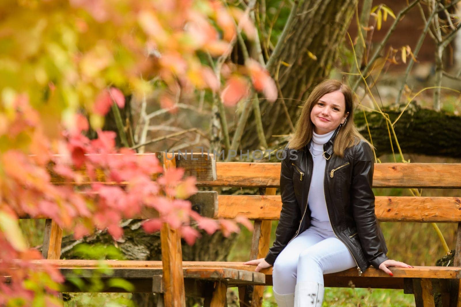 A young beautiful girl sits on a bench in an autumn park a