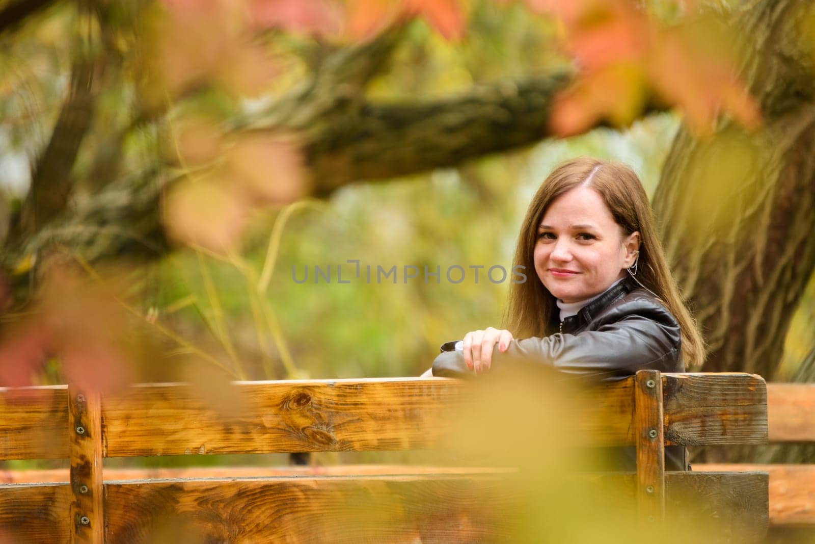 A young beautiful girl sits on a bench in an autumn park and turns around and looks into the frame a