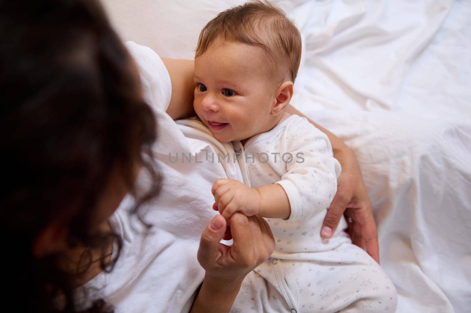 View from above of a Latin woman embracing her baby boy, holding him in her arms. Cute newborn child smiles to his mother. Copy space. Family relationships. Mother and son together. Love and care