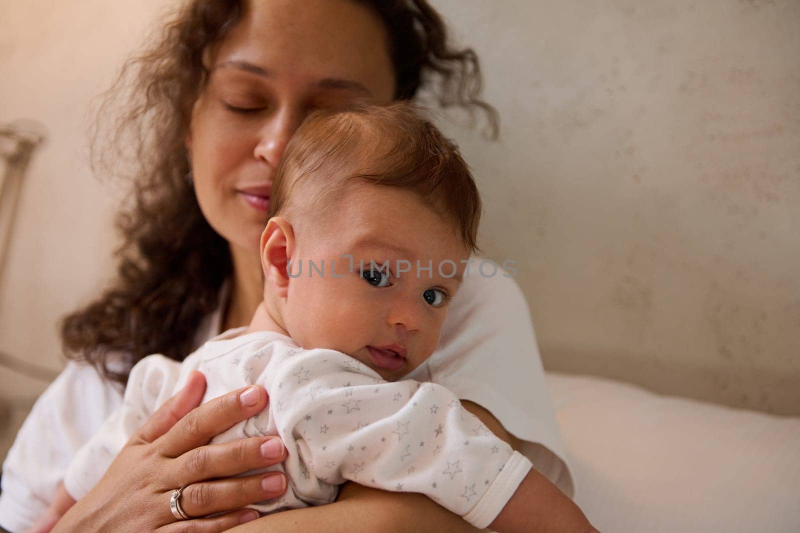 Selective focus adorable Caucasian child, newborn baby in the hands of delightful Latin American young adult blur woman, happy loving mother gently hugging her baby boy. Infancy and maternity concept