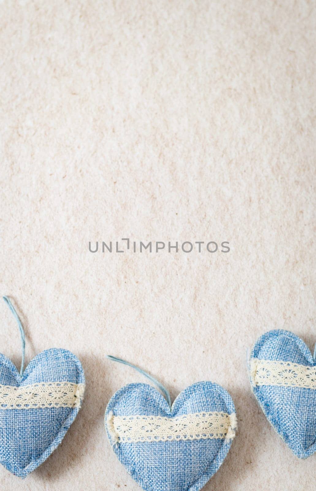 Three blue textile hearts with openwork stripes lie from below on a beige stone background with copy space on top, flat lay close-up. The concept of valentine's day, love day.