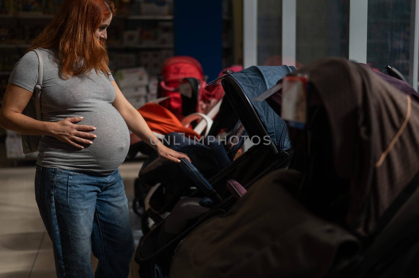 Red-haired pregnant woman chooses a stroller in a children's store
