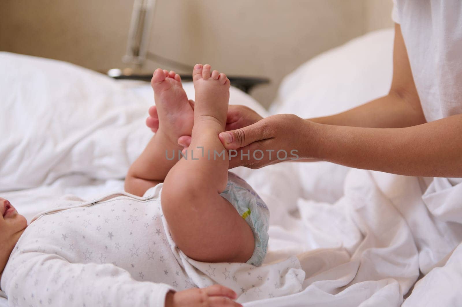 Close-up hands of a unrecognizable woman mother holding baby legs and doing gentle massage movements to prophylaxis the flat feet and orthopedic diseases. Pediatrics. Healthcare and medicine