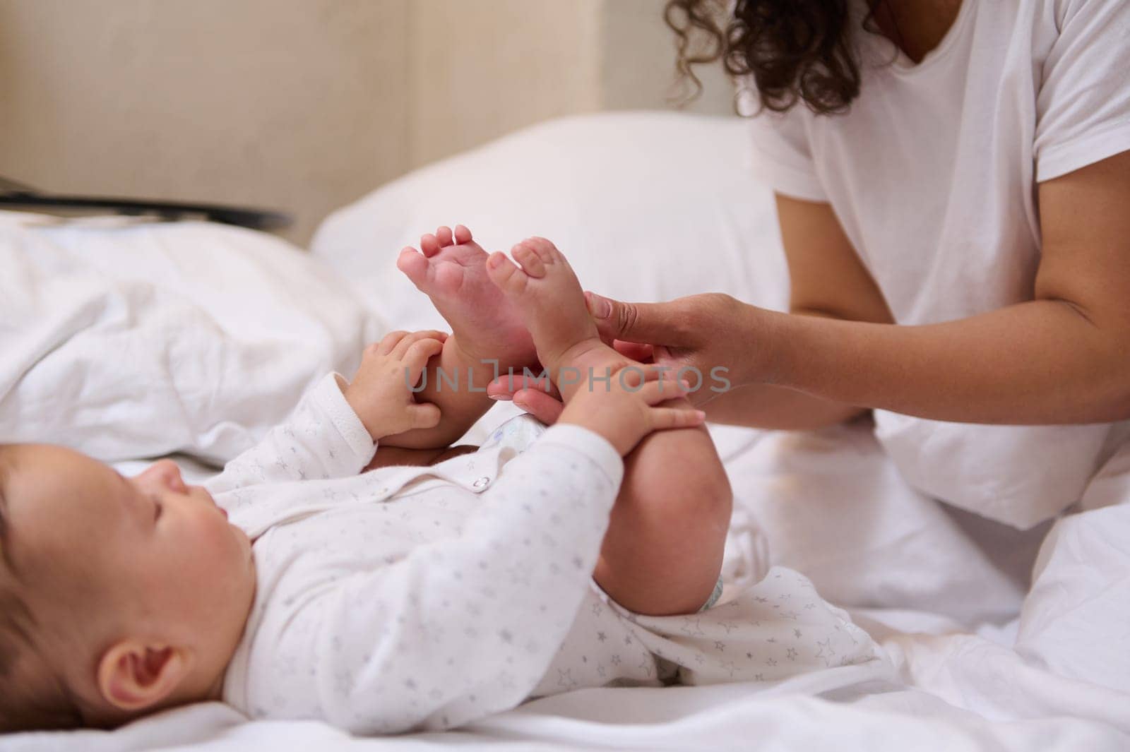 Close-up young mother massaging feet and toes of her newborn baby, enjoying happy time together Baby care and infancy by artgf