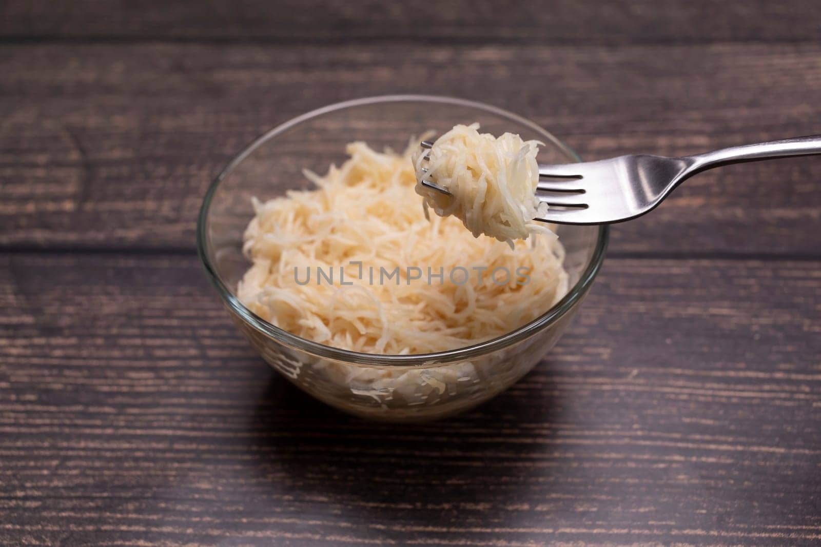 Homemade Fermented Celeriac Salad on Fork Above Glass Bowl. Preserved Vegetable On Table. Superfood, Harvesting, Nutrition Source. Shredded And Pickled Celery Crops, Tuber. Culinary. Horizontal Plane