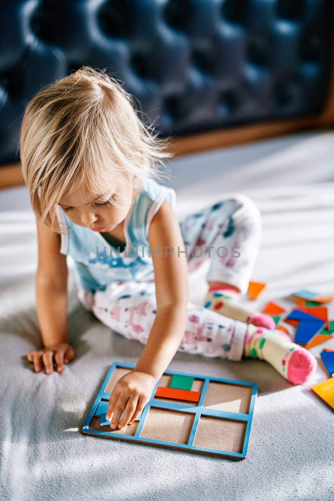 Little girl sits on the bed and puts together a puzzle. High quality photo