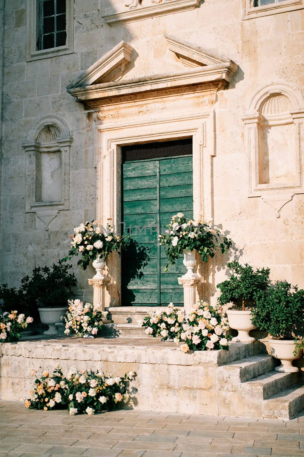 Wedding semi-arch with bouquets of flowers stands on the steps of St. Mark Church. Perast, Montenegro. High quality photo