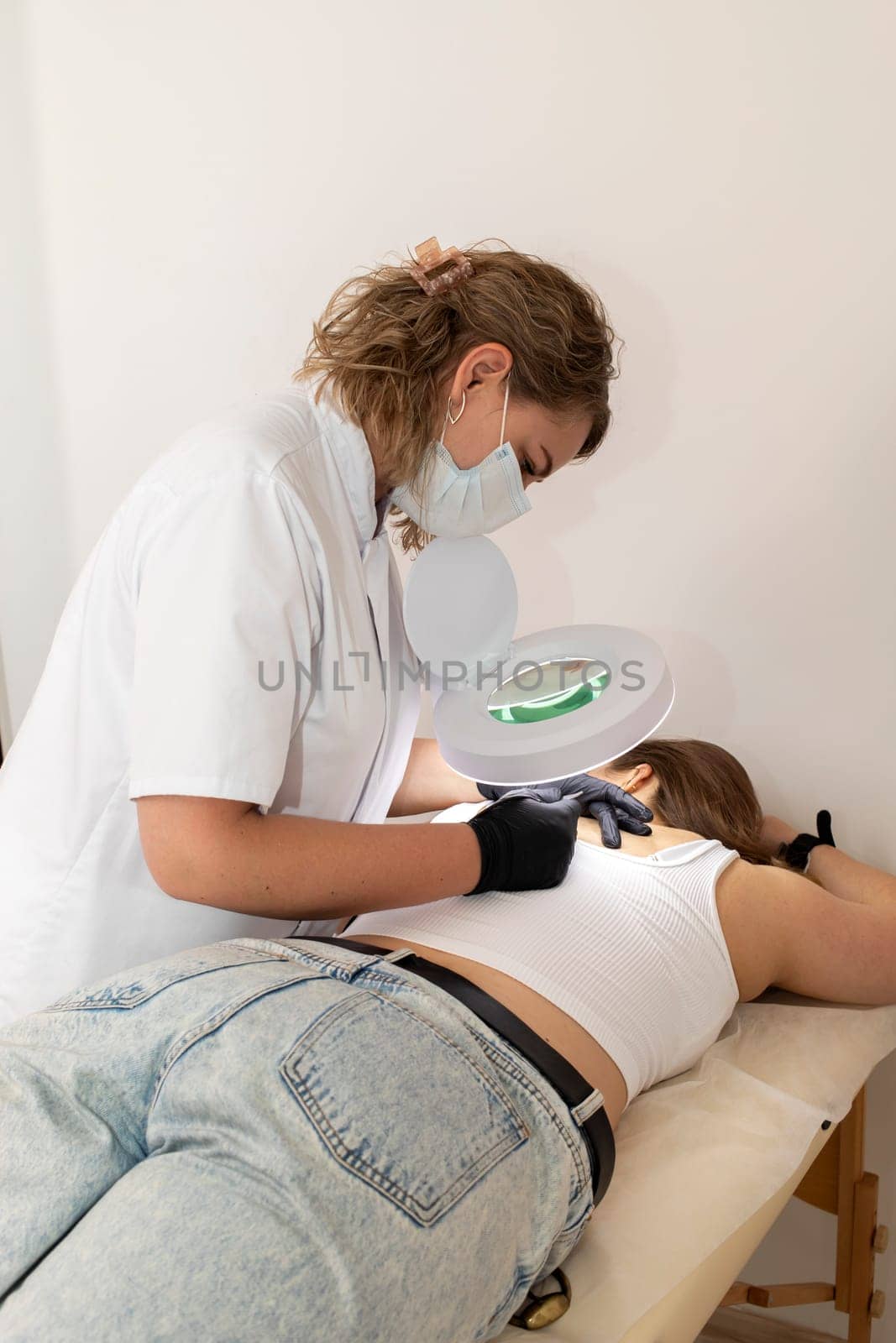 Doctor Doing Hair Removal Electrolysis Procedure On Woman's Back, Electric Epilation In Beauty Salon. Vertical Plane. Authentic Photo High quality photo
