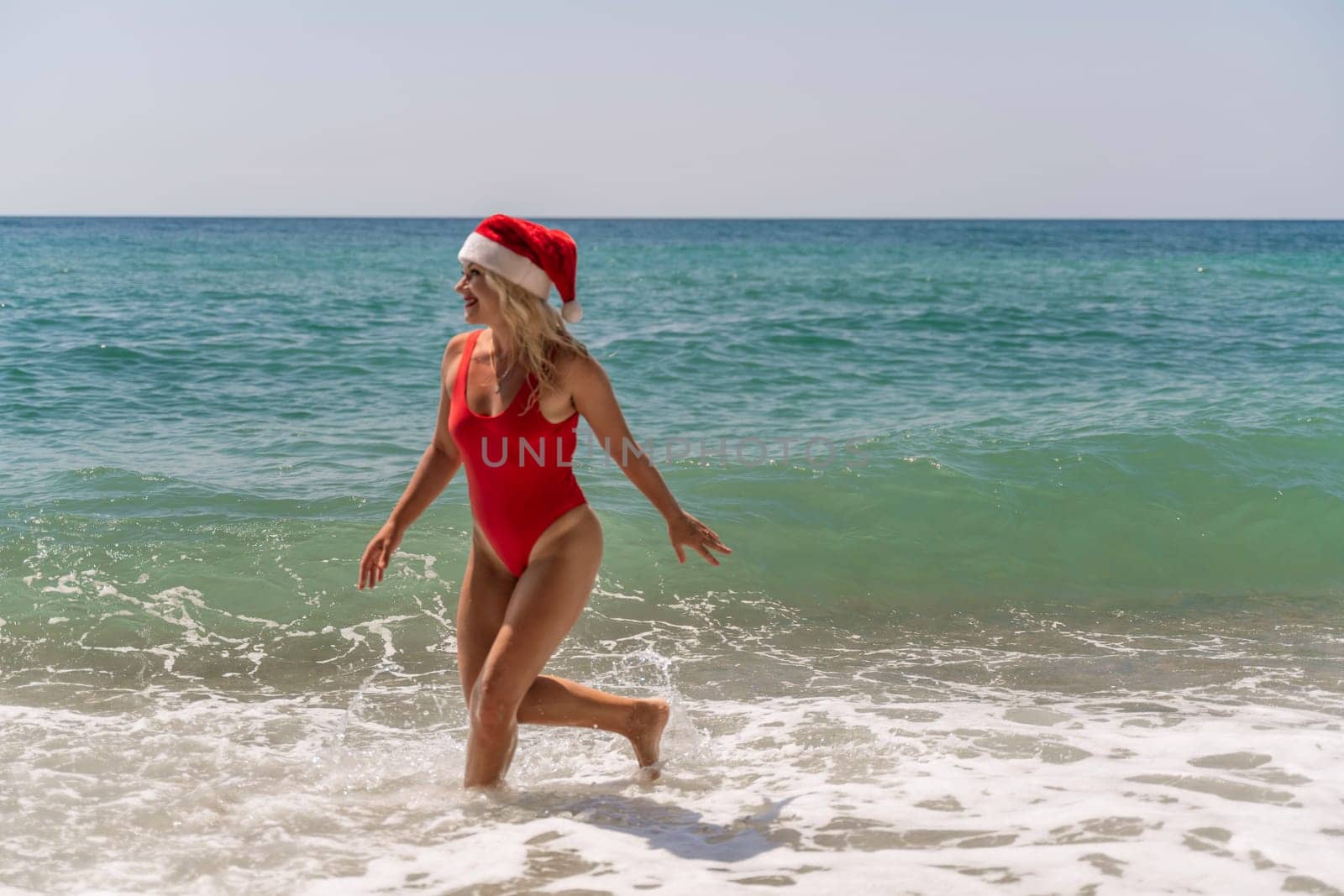 A woman in Santa hat on the seashore, dressed in a red swimsuit. New Year's celebration in a hot country.