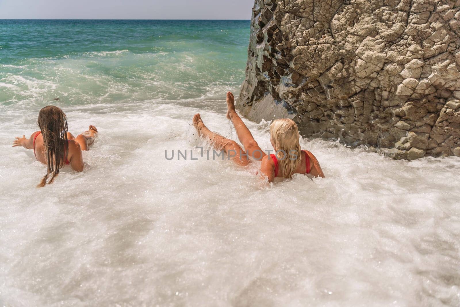 Women ocean play. Seaside, beach daytime, enjoying beach fun. Two women in red swimsuits enjoying themselves in the ocean waves