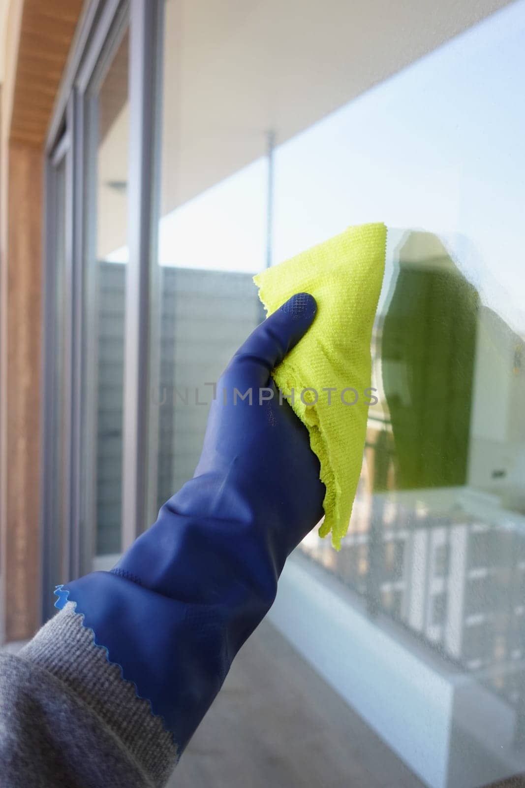 hand in blue glove cleaning window with green rag by towfiq007